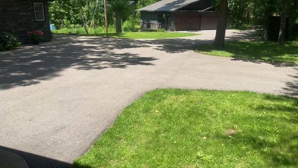 Quiet suburban driveway and lawn beside a house under trees on a sunny day