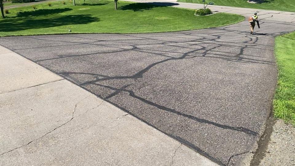 Cracked asphalt path beside a sidewalk and grass, with a person walking in the distance.