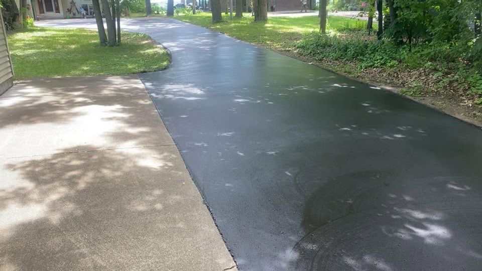 Wet paved path curving through a green park with trees and grass
