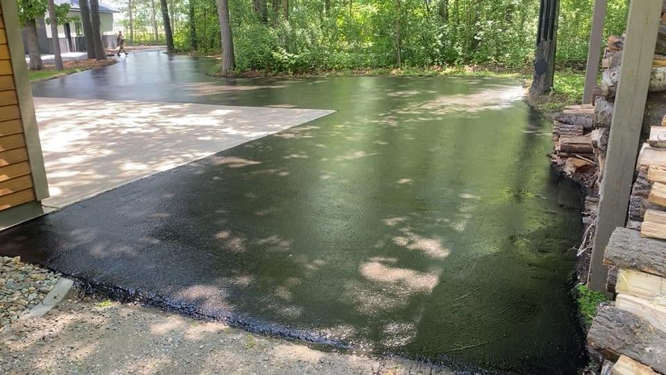 Flooded driveway beside a house, with standing water reflecting trees and sunlight.