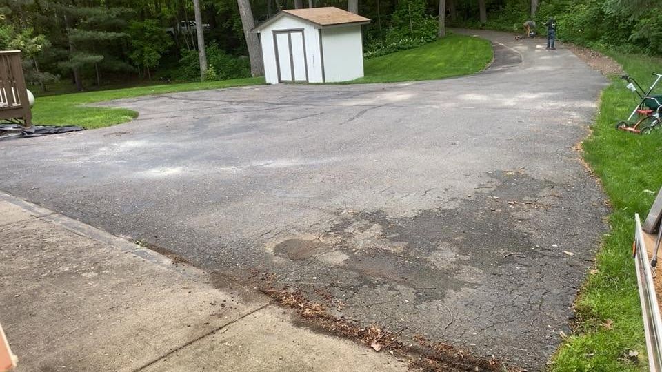 Gravel driveway curves past a small white shed beside a wooded area.