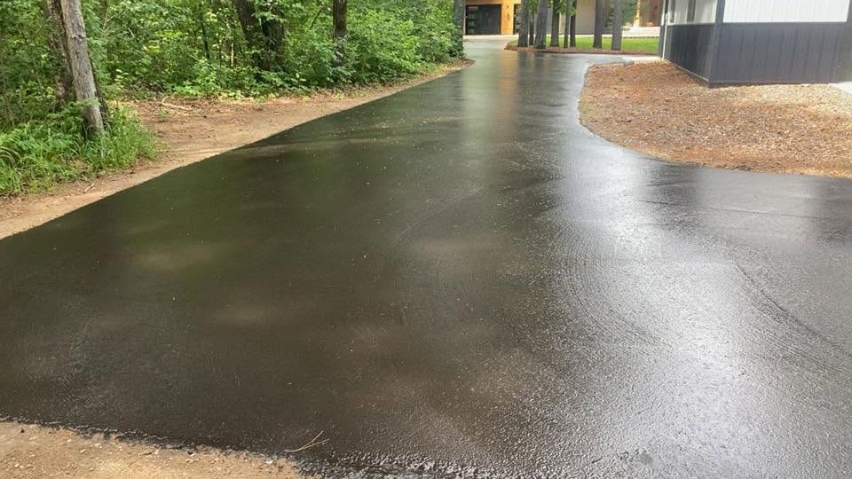 Rainy wet asphalt path beside green trees and a building entrance