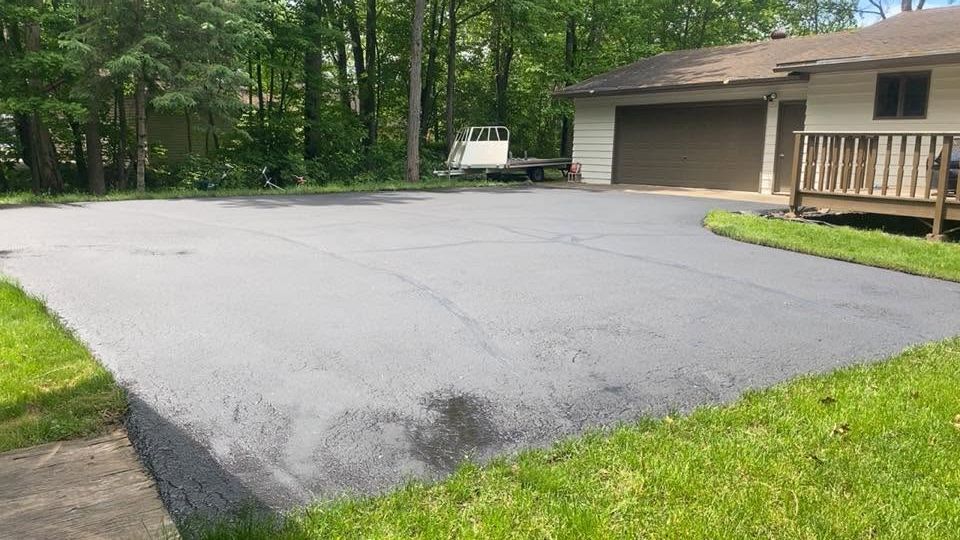 Freshly paved driveway beside a garage, bordered by green grass and trees