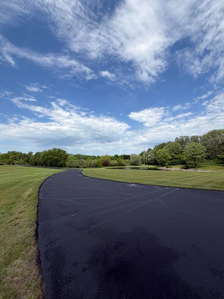 Curving black paved path through a green park under a blue sky with scattered clouds