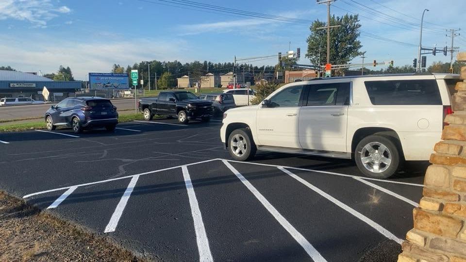 Parking lot with a white SUV beside a crosswalk and a black sedan in the background.