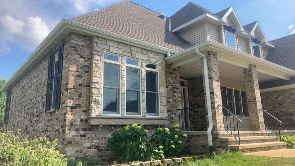 Stone suburban house with beige trim, front porch, and large windows on a sunny day