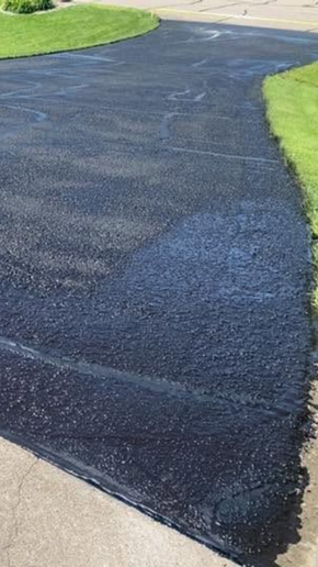 Freshly paved black asphalt driveway bordered by bright green grass and a concrete edge