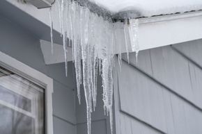 Icicles hanging from a house roof over gray siding and a window
