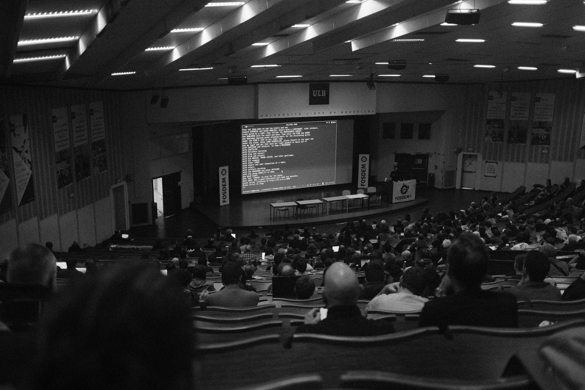 Auditorium lecture hall with a large projected screen and seated audience in dim lighting