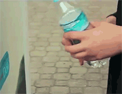 Hands twisting a plastic water bottle near a white object with a blue sticker, outdoors.