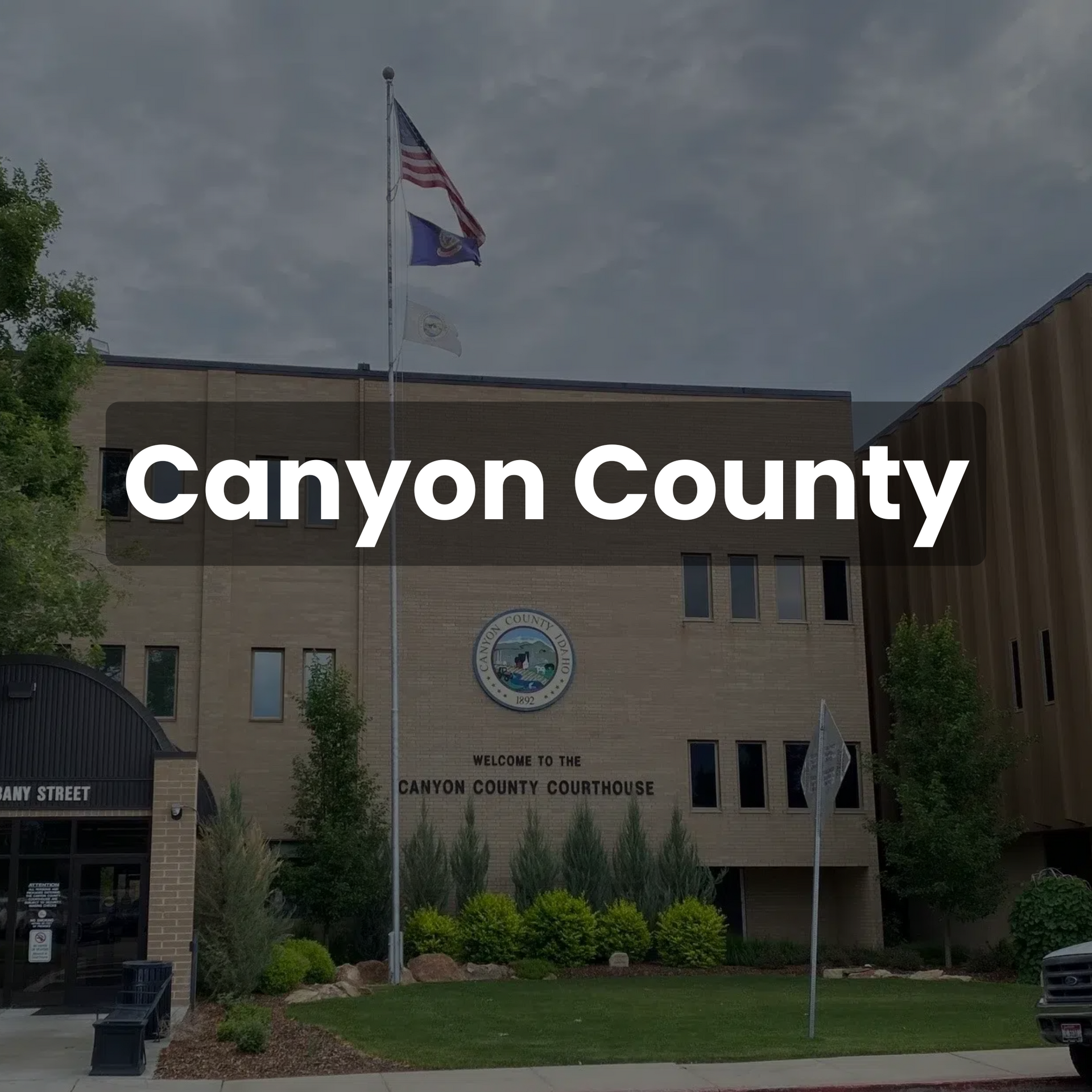 Canyon County building with US and Idaho flags; cloudy sky.