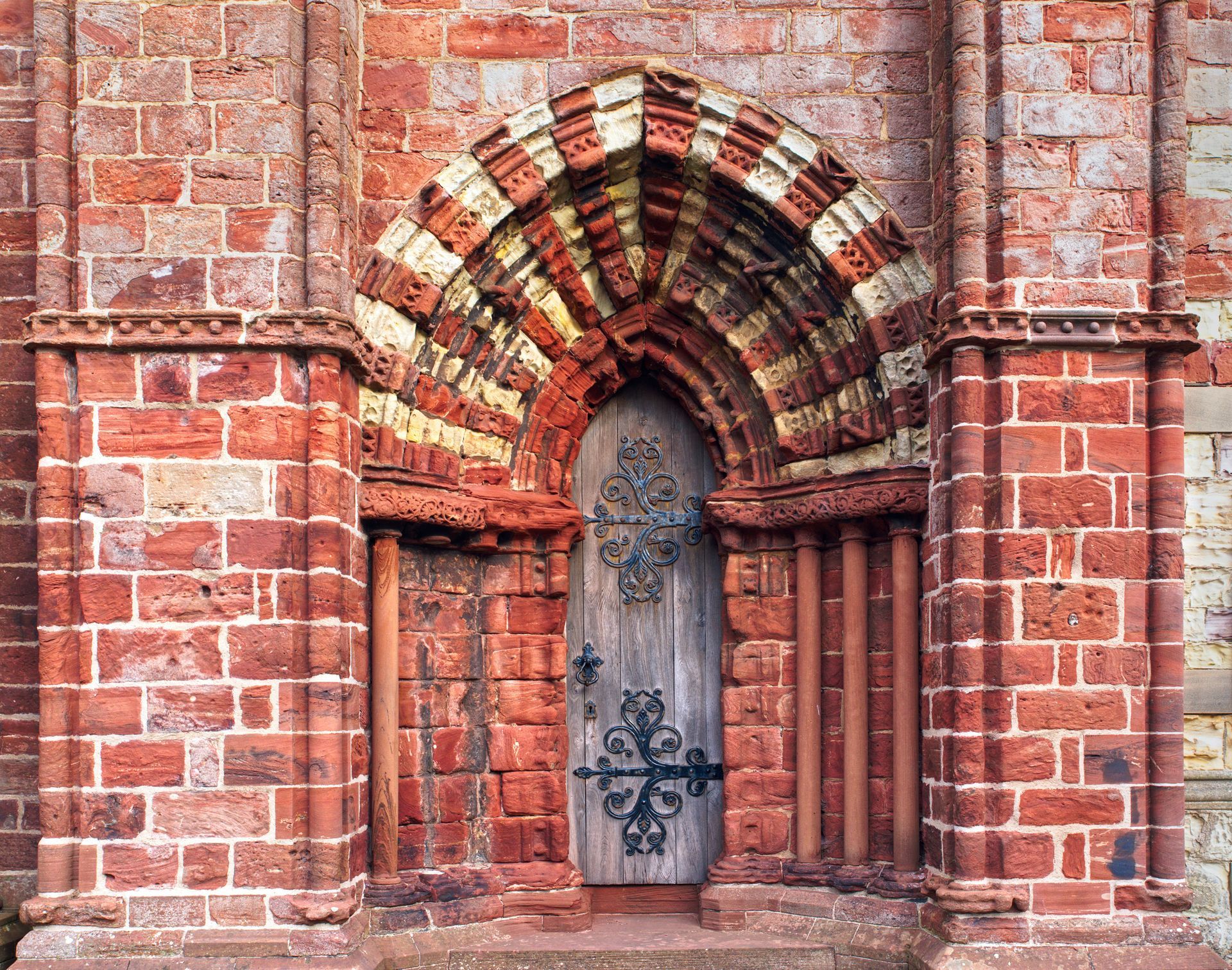 Red brick archway and door with ornate metal hinges.