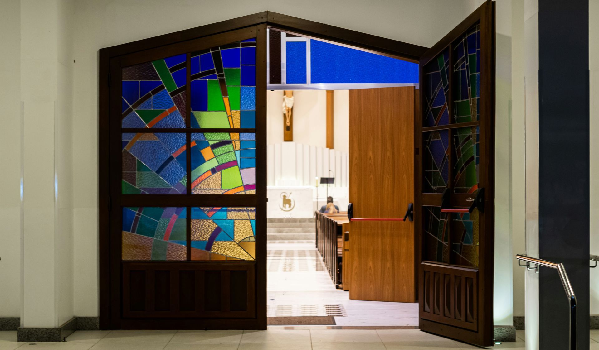 Open church doors with stained glass, revealing an interior with pews, altar, and crucifix.