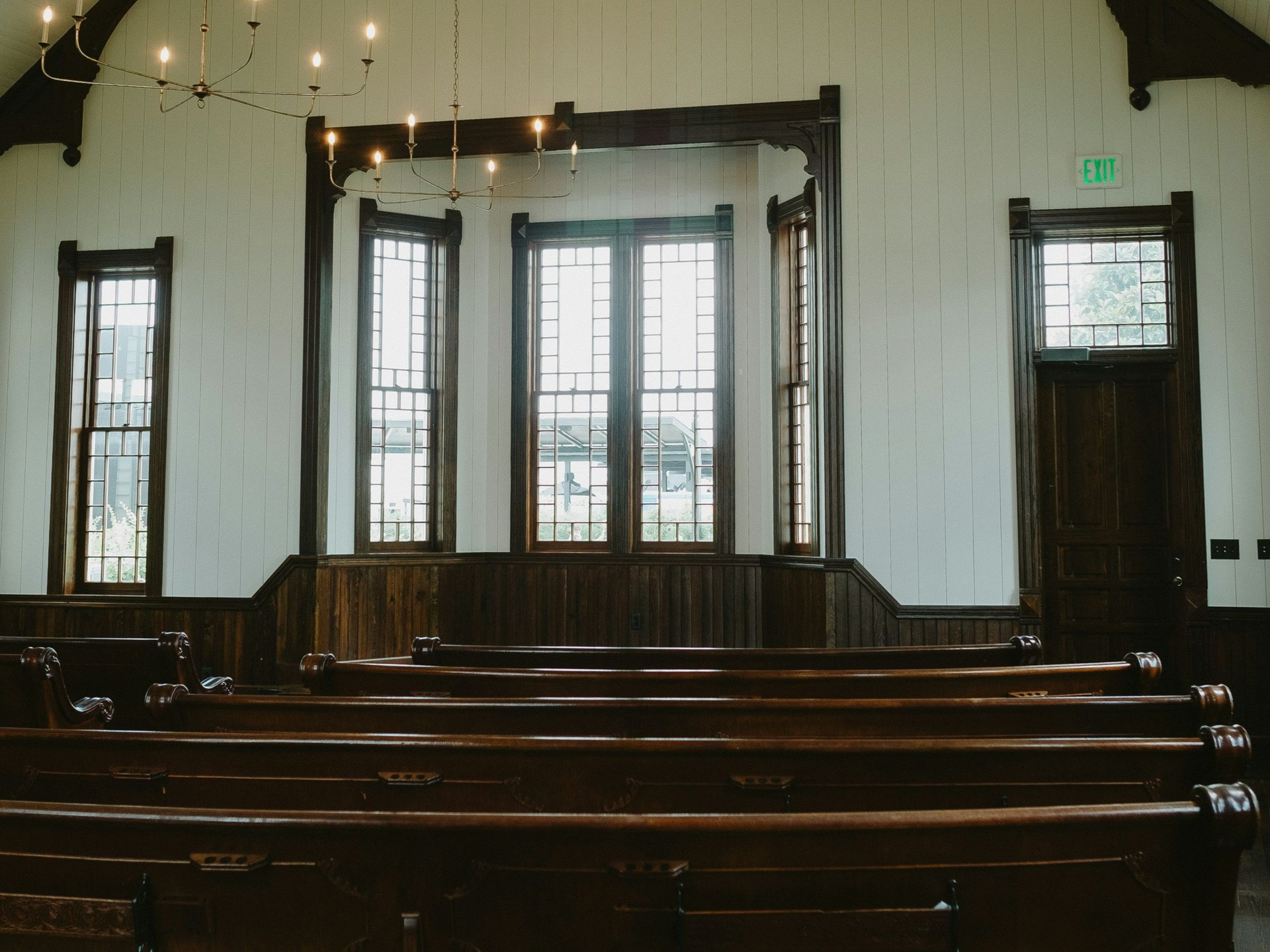 Church interior with wooden pews, windows, and decorative trim. Sunlight streams through the windows.