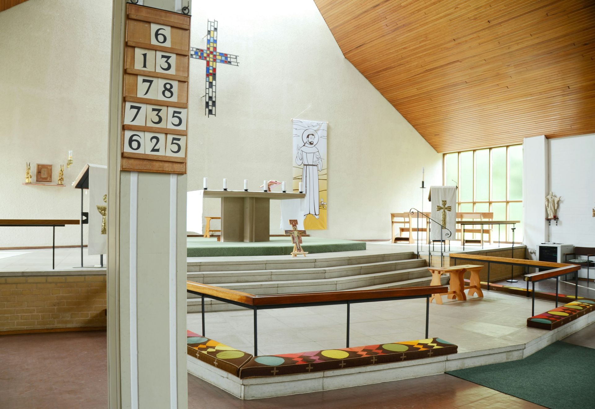 Interior view of a church. Features an altar, pews, a large cross, and a wooden ceiling.