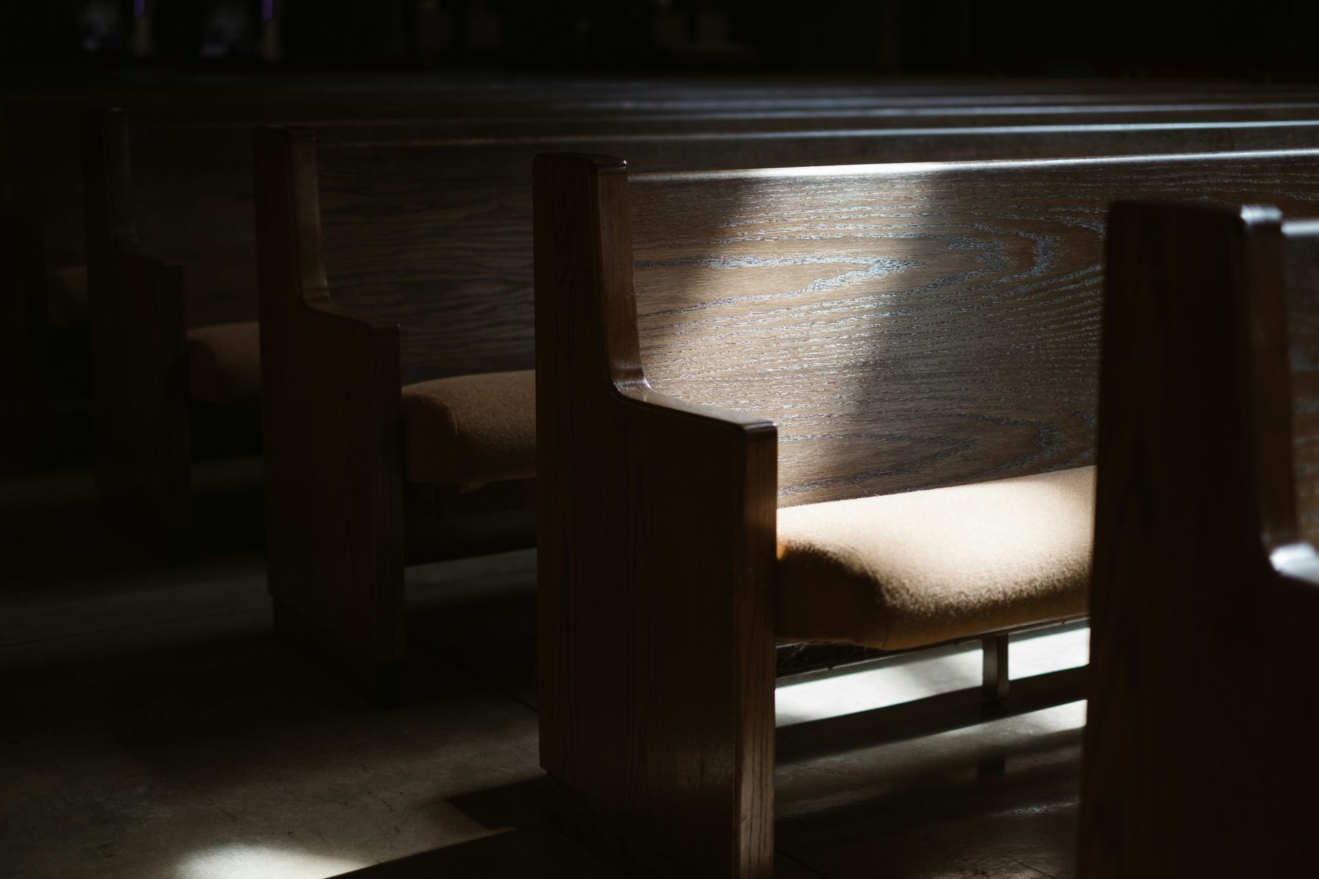 Wooden church pews with light streaming across them from an unseen window.