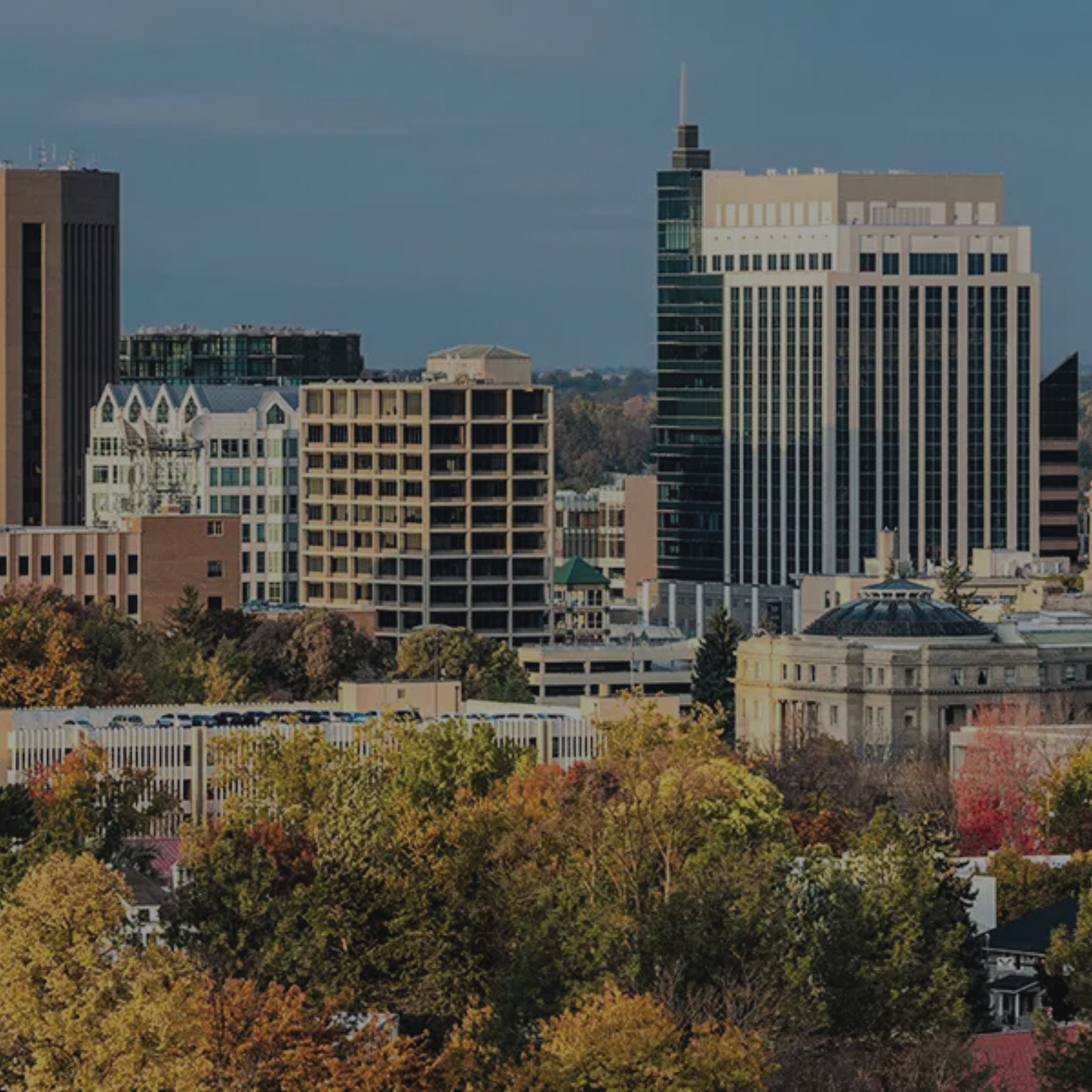 Boise City skyline with tall buildings, trees with fall foliage, and a blue sky.