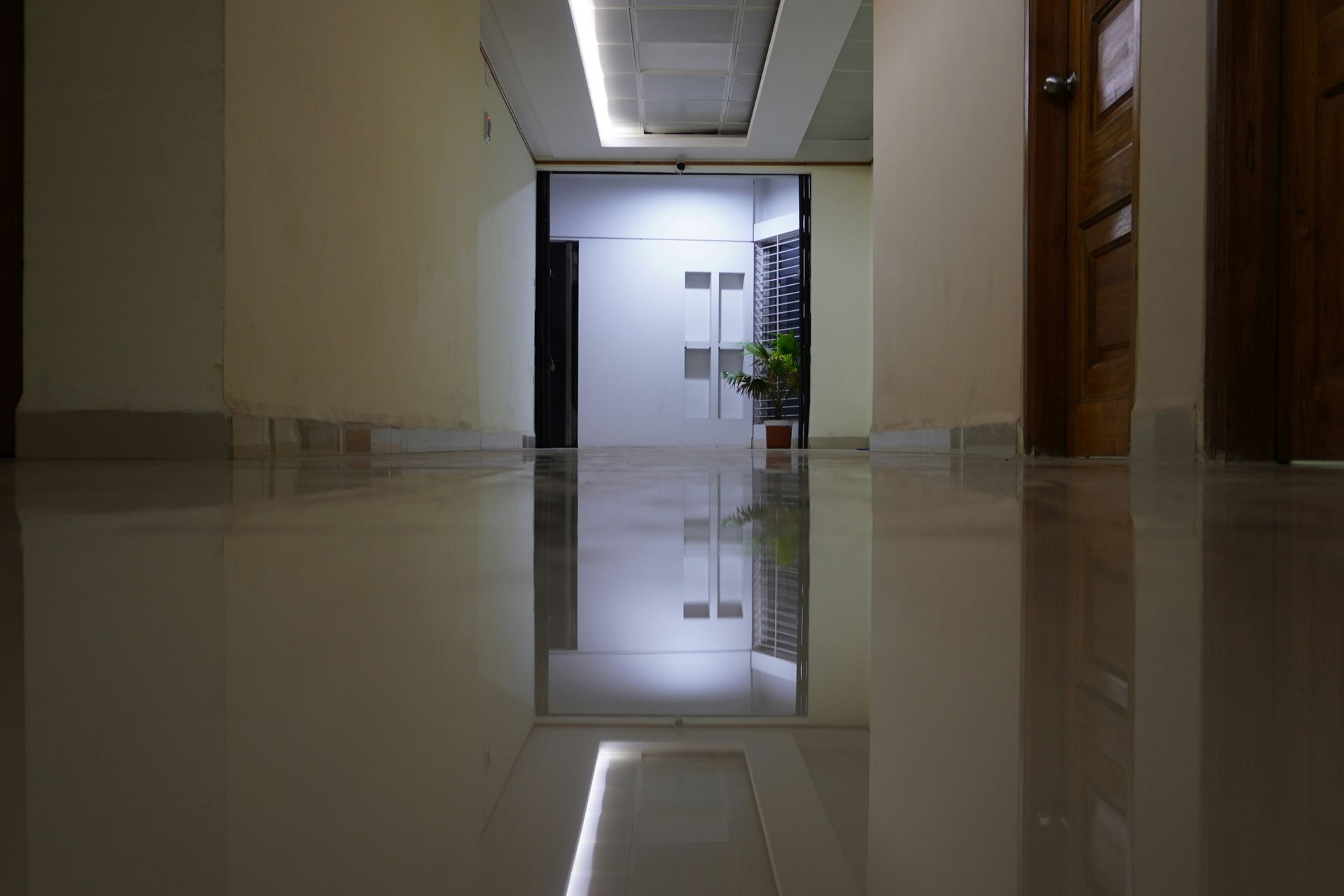 A long, empty hallway with a glossy floor reflecting overhead lights and open doorway at the end.