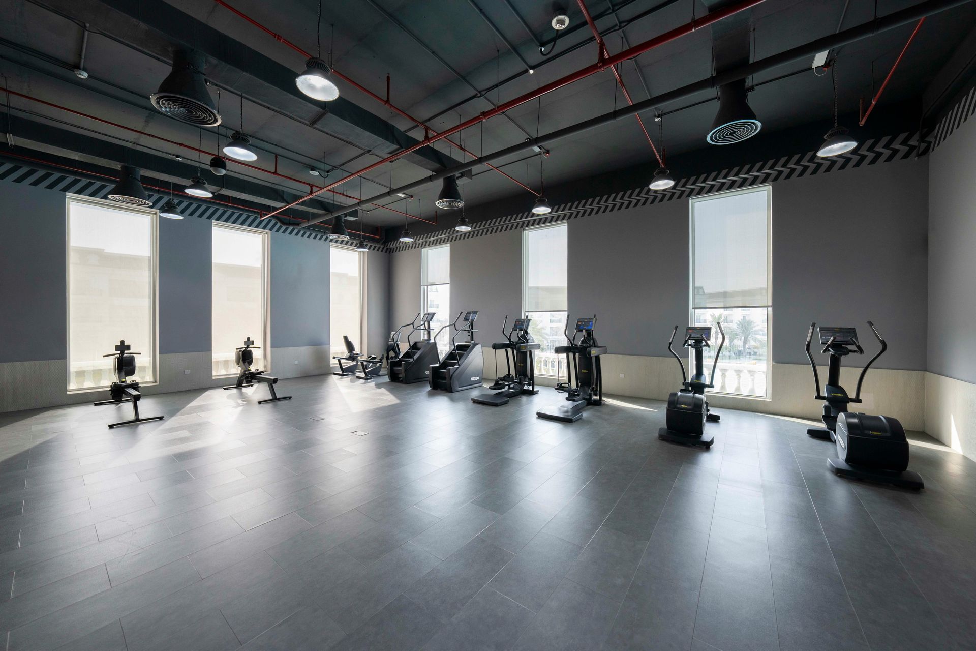 Gym interior with exercise machines, windows, and dark ceiling.