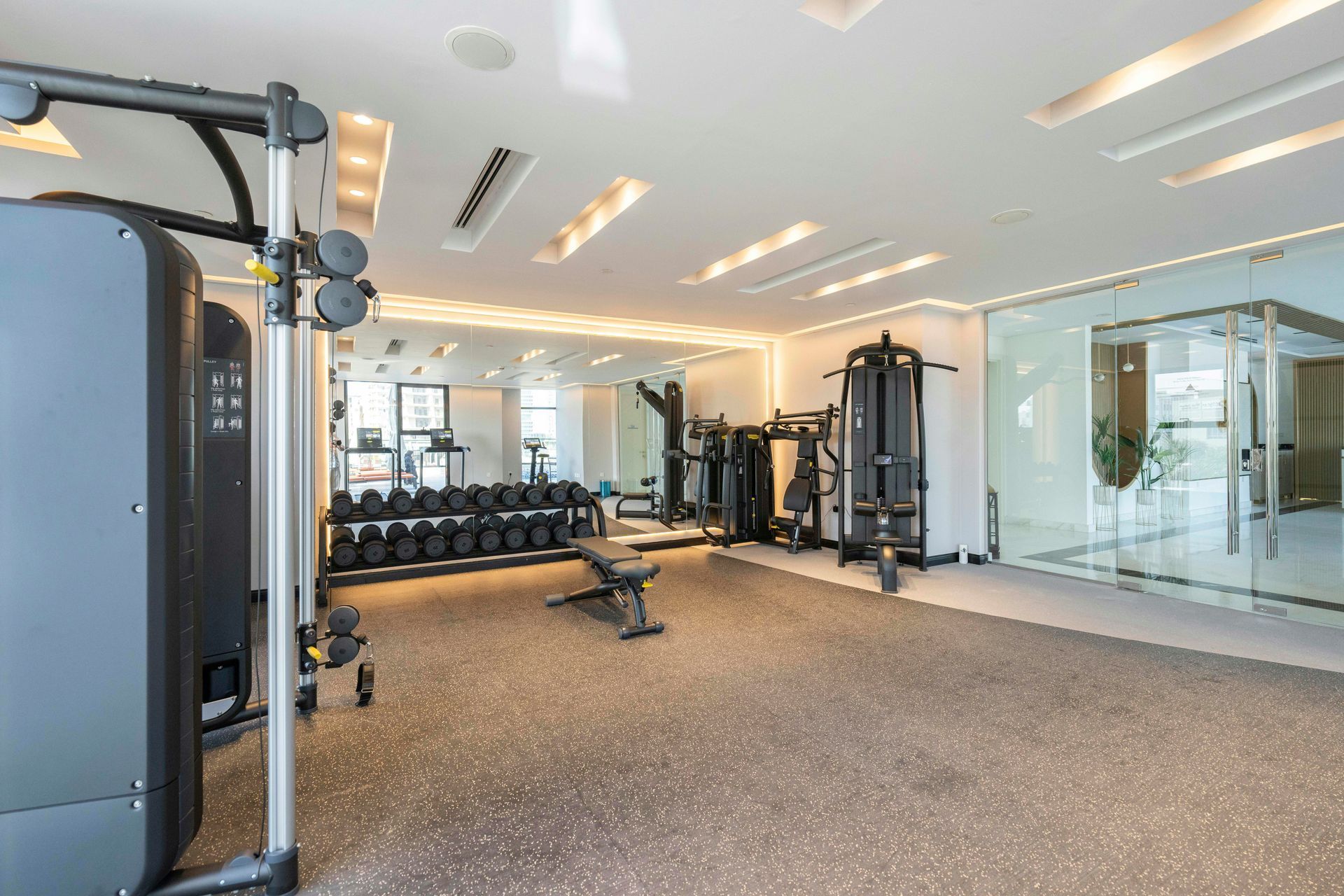Gym interior with weight machines, dumbbells, mirror, and rubber flooring.