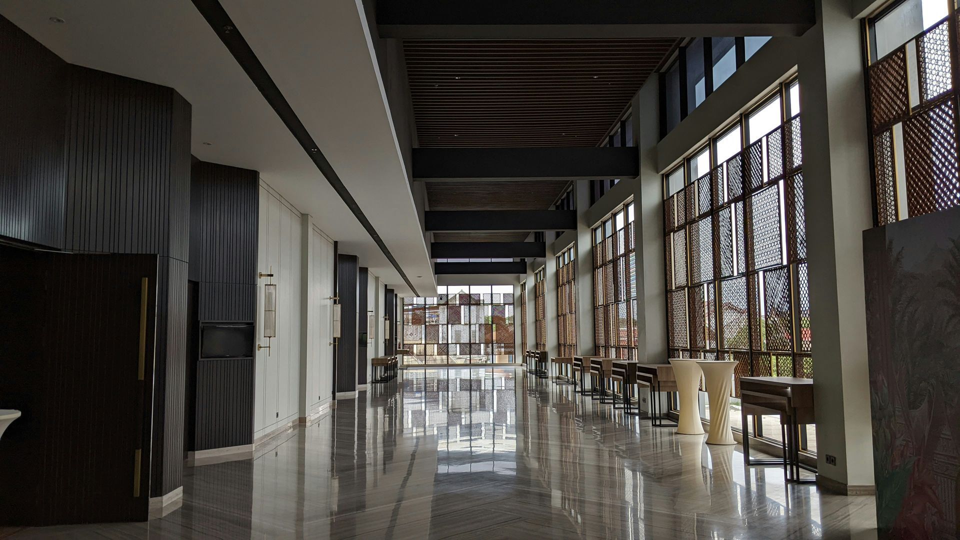 Long hallway with large windows, tables, and textured walls.