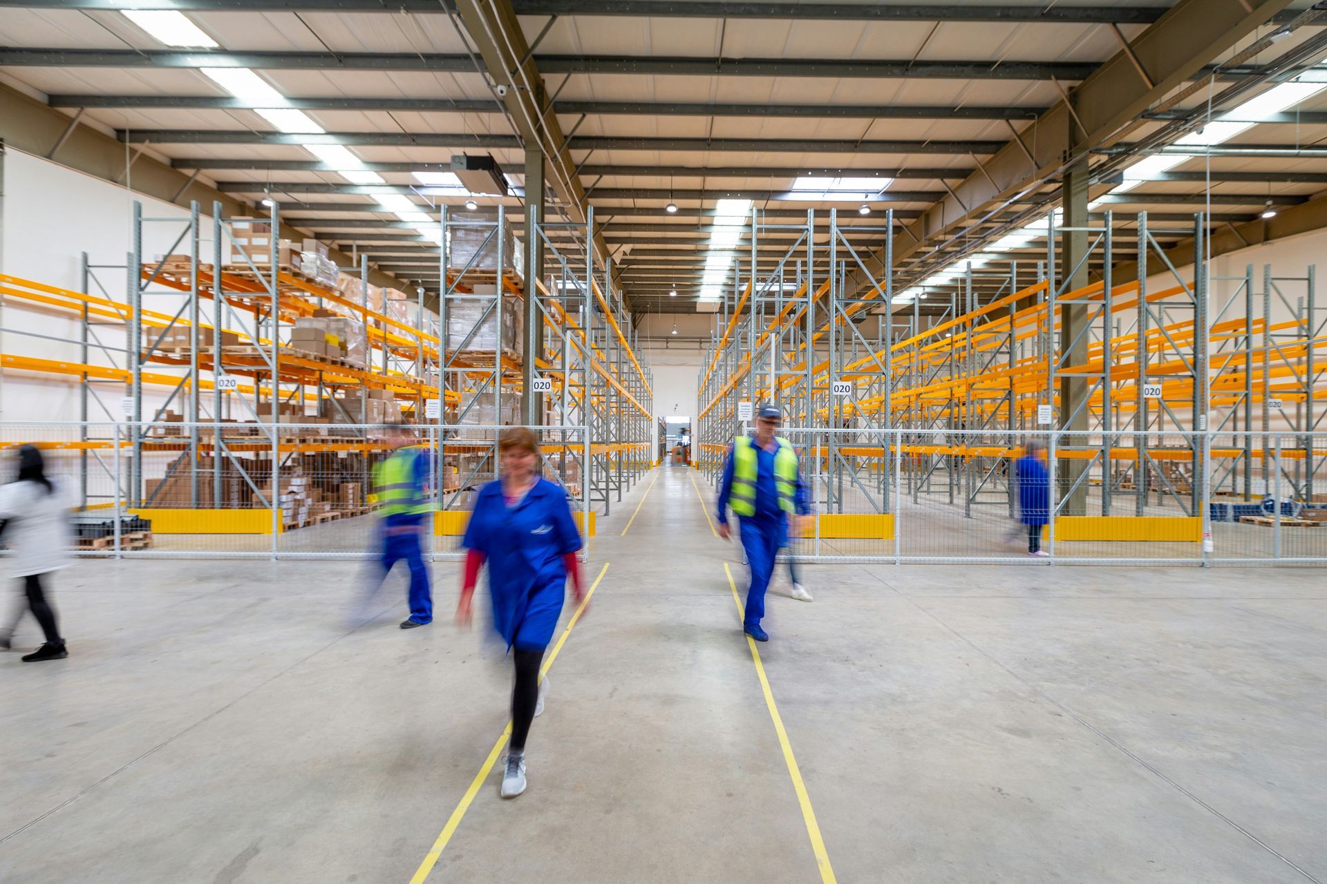 Warehouse interior with workers, yellow shelving units, and yellow floor lines.
