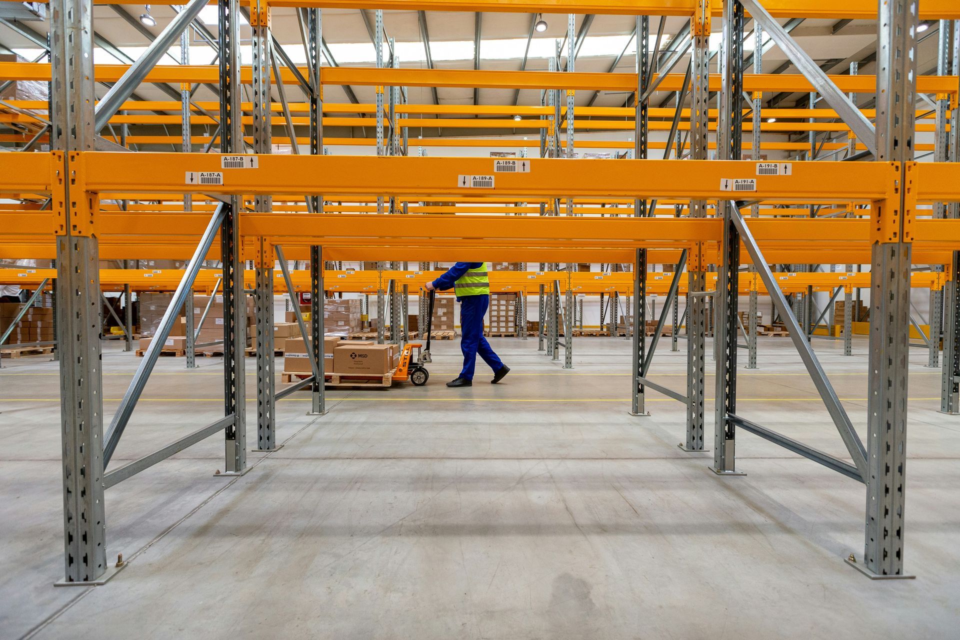 Warehouse interior with rows of yellow shelving and worker using a pallet jack.