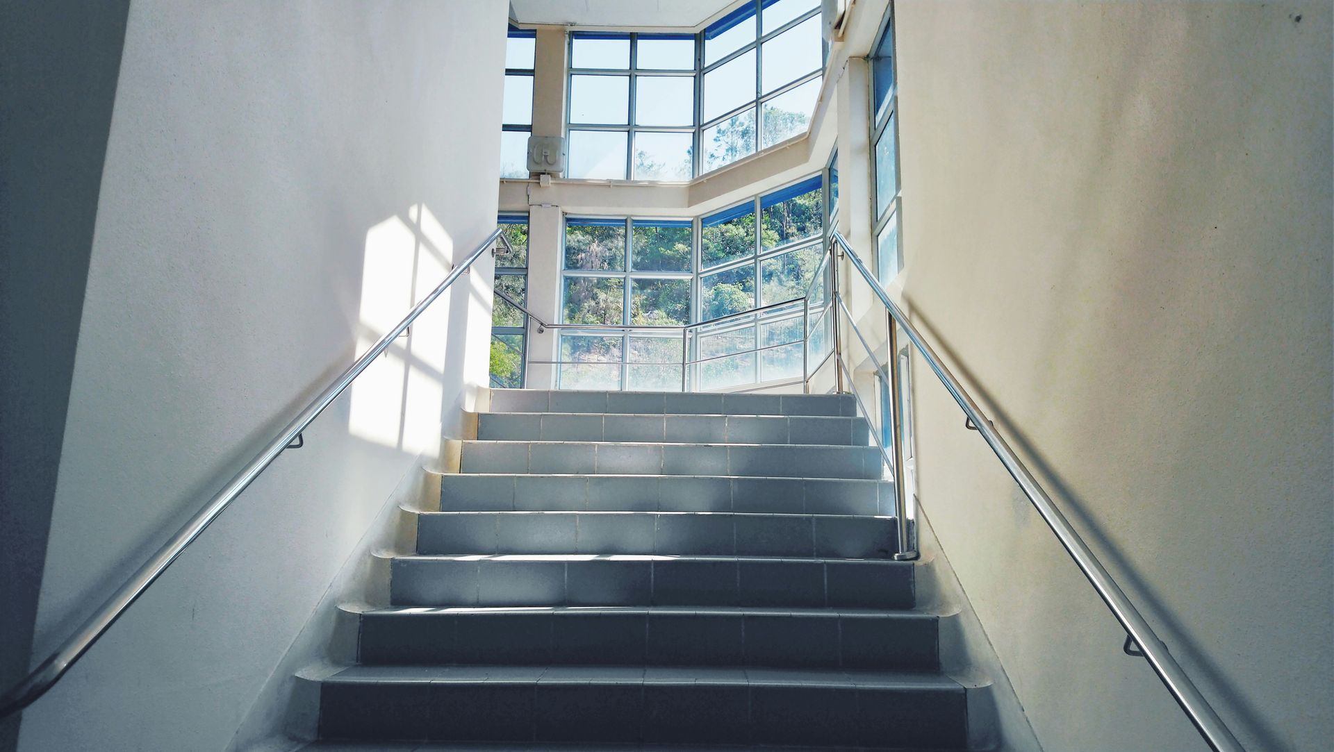 Staircase leading upwards to a windowed landing, with sunlight illuminating the steps.