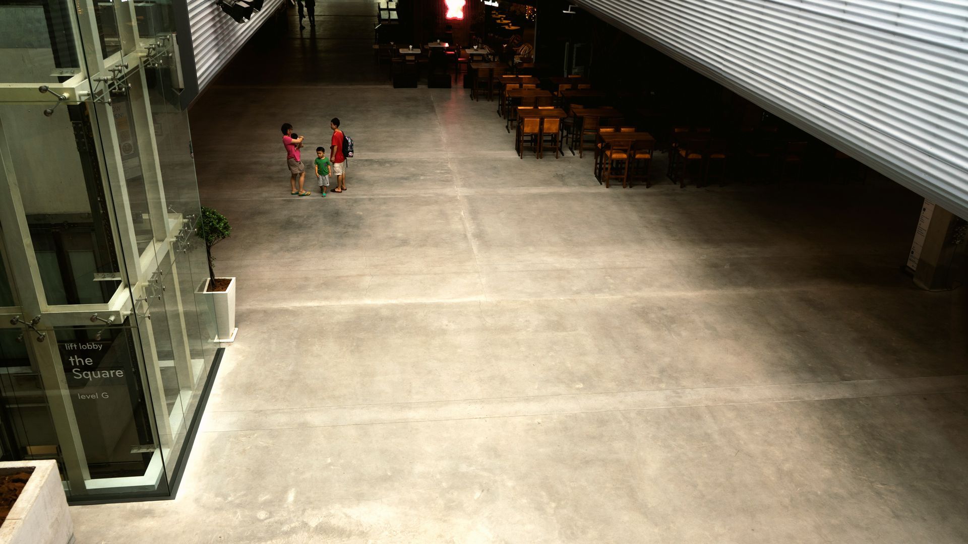 A family of three walking through a mall corridor with cafe seating and large windows.
