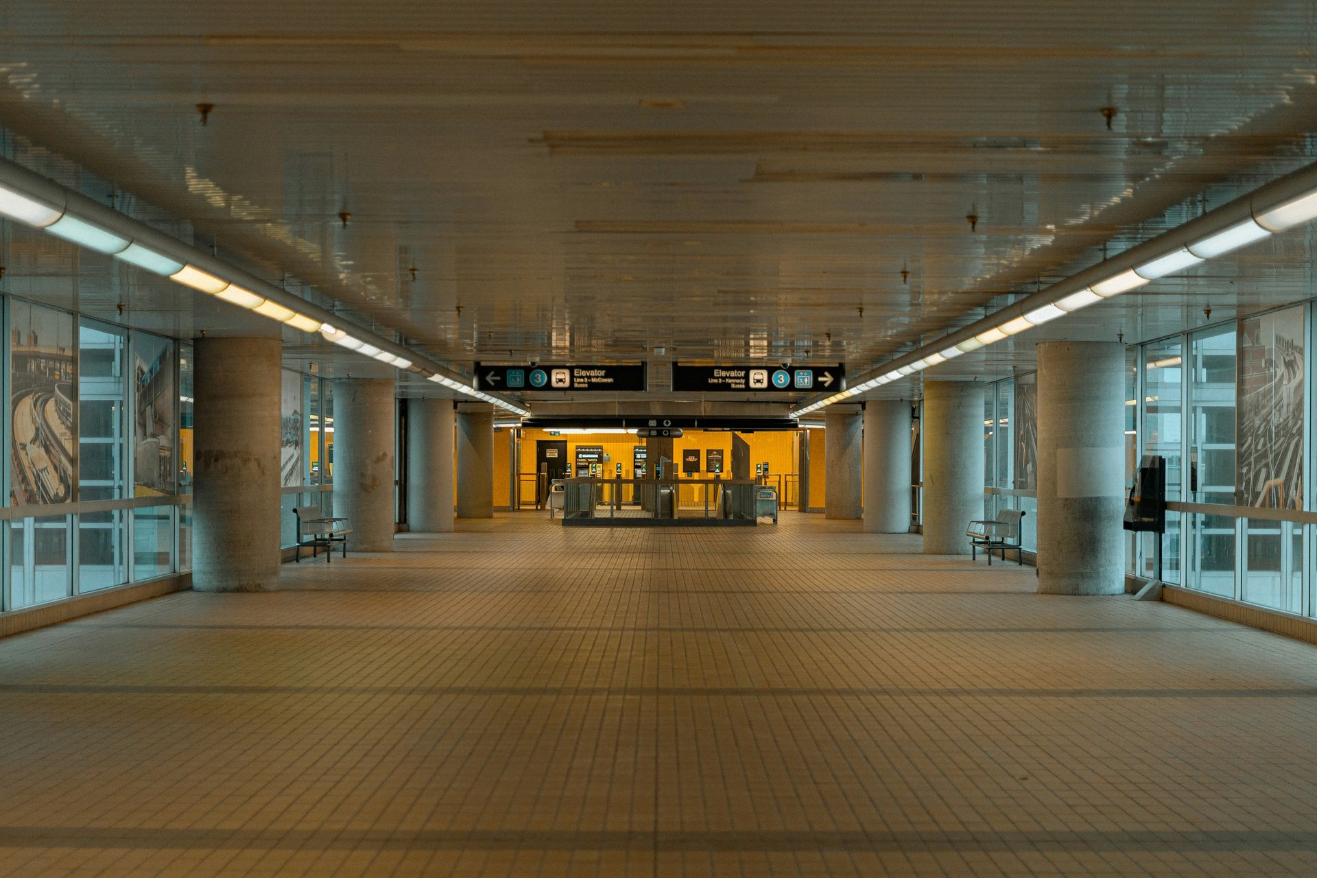 Hallway in a subway station with columns and signs, well-lit with fluorescent lights.