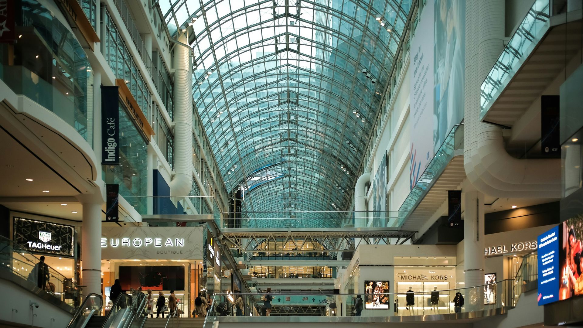 Interior view of a modern shopping mall with a glass ceiling and multiple levels of stores.