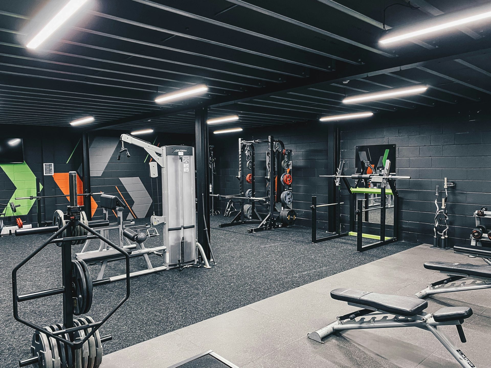 Interior of a gym with weightlifting equipment; black ceiling and walls, gray floor, bright overhead lights.