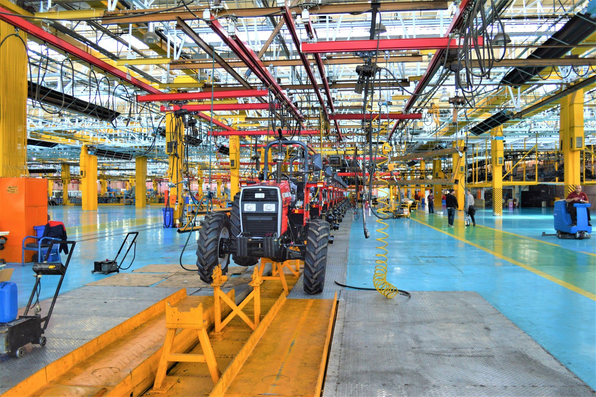 Tractor assembly line in a factory. Red and black tractor on a yellow platform. Overhead lighting and machinery.