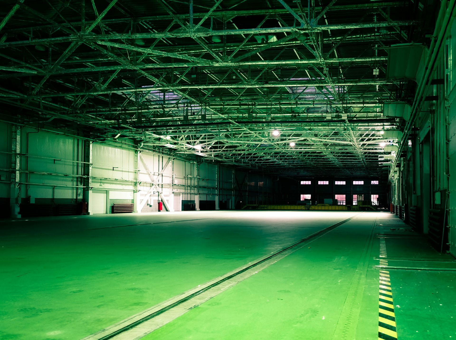 Large, empty warehouse interior, lit with green hues. Metal ceiling, concrete floor, loading docks.
