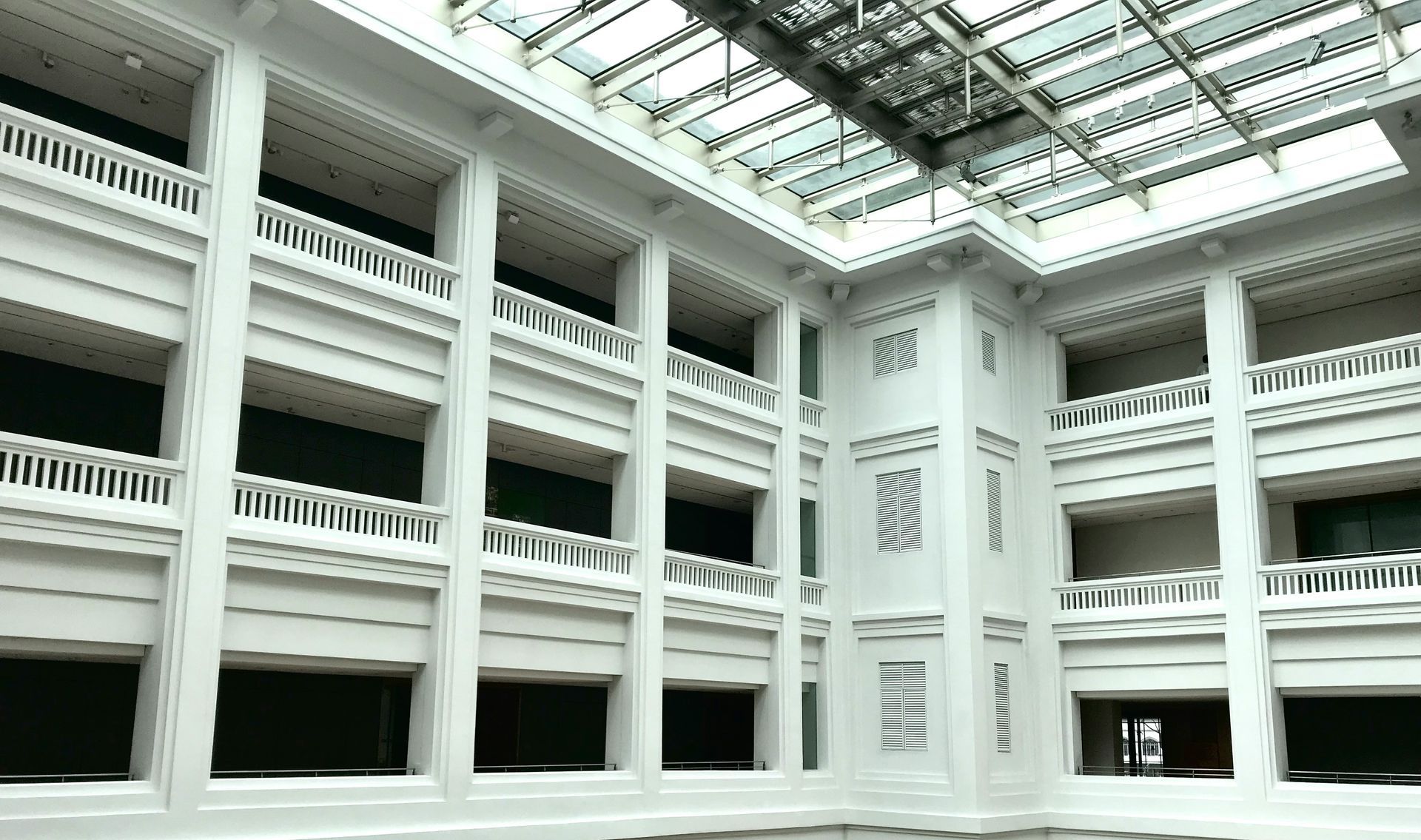 Interior of a white building with pillars, balconies, and a glass ceiling.