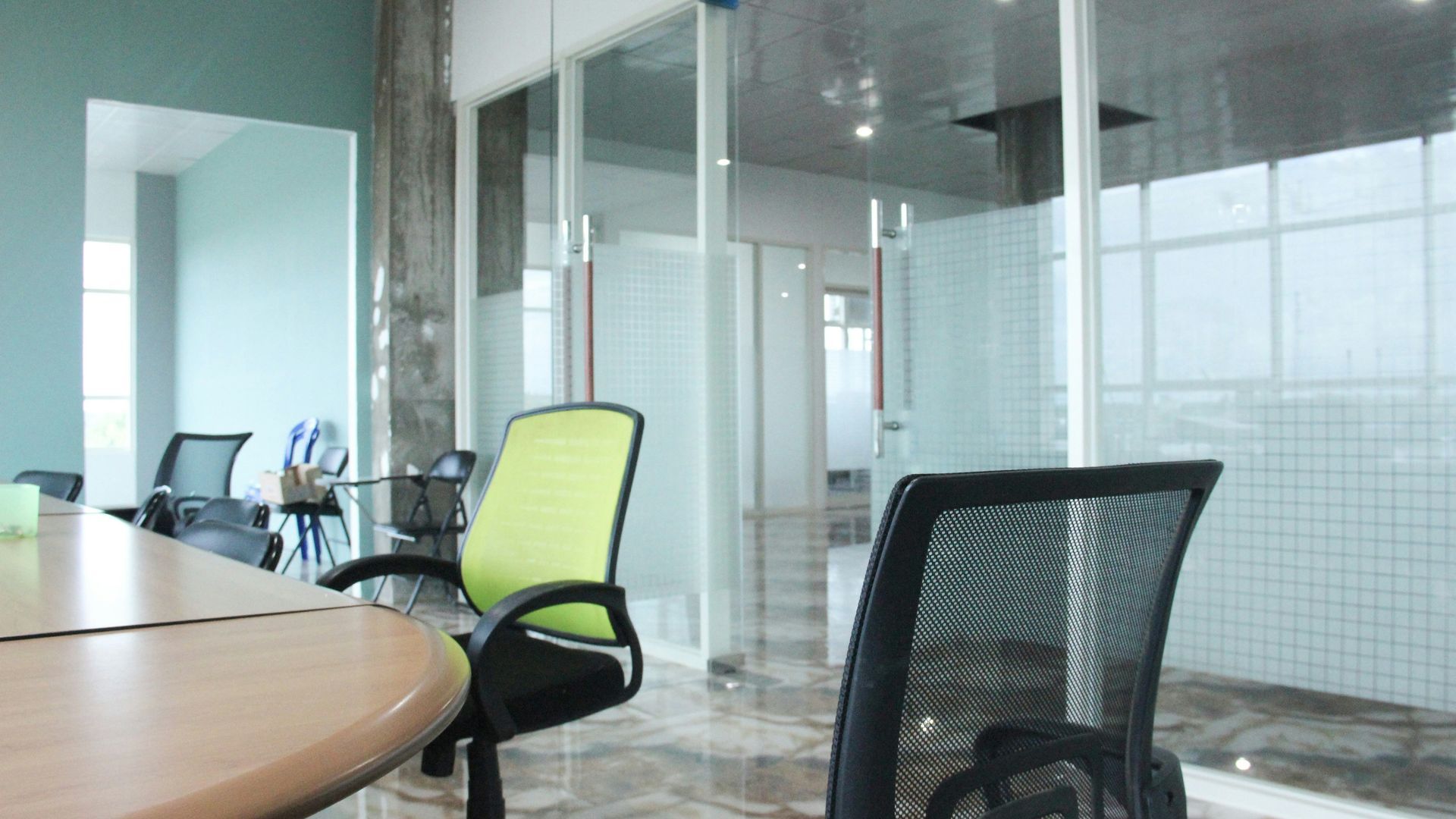 Office interior with conference table, chairs, and glass-walled rooms. One chair is green.