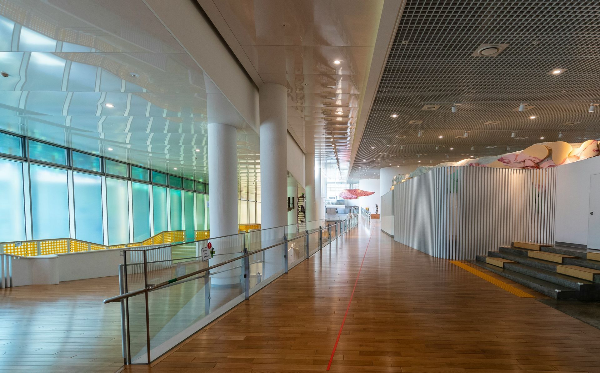 Hallway with glass windows, white columns, wooden floor, and decorative panels.