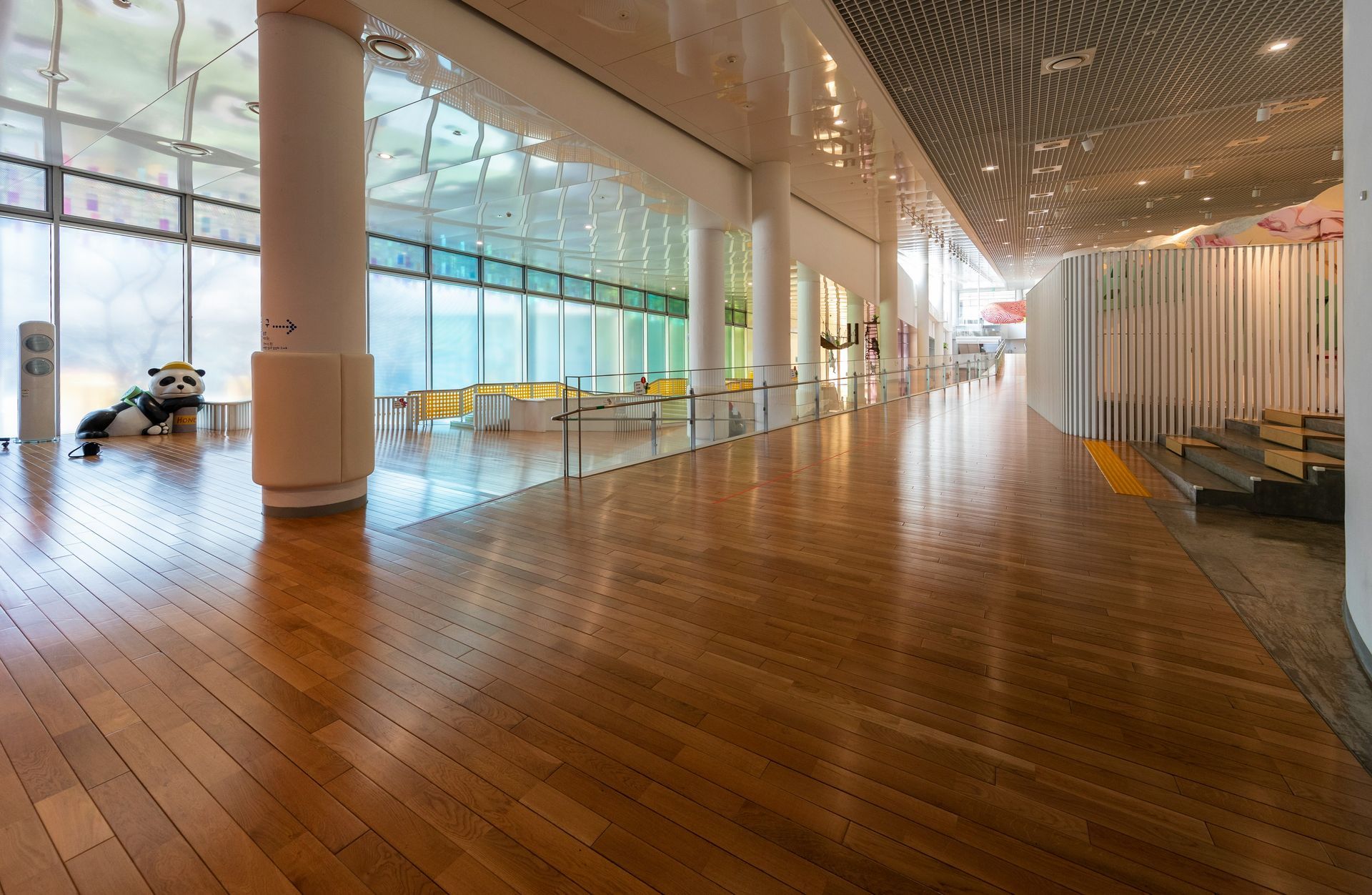 Wooden floor hallway with large windows, white columns, and a panda statue.