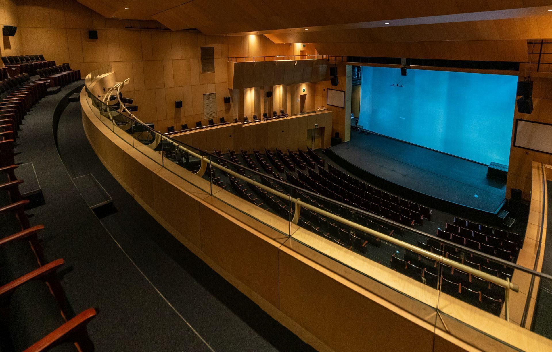 Empty theater auditorium with rows of seats facing a stage with a blue backdrop.