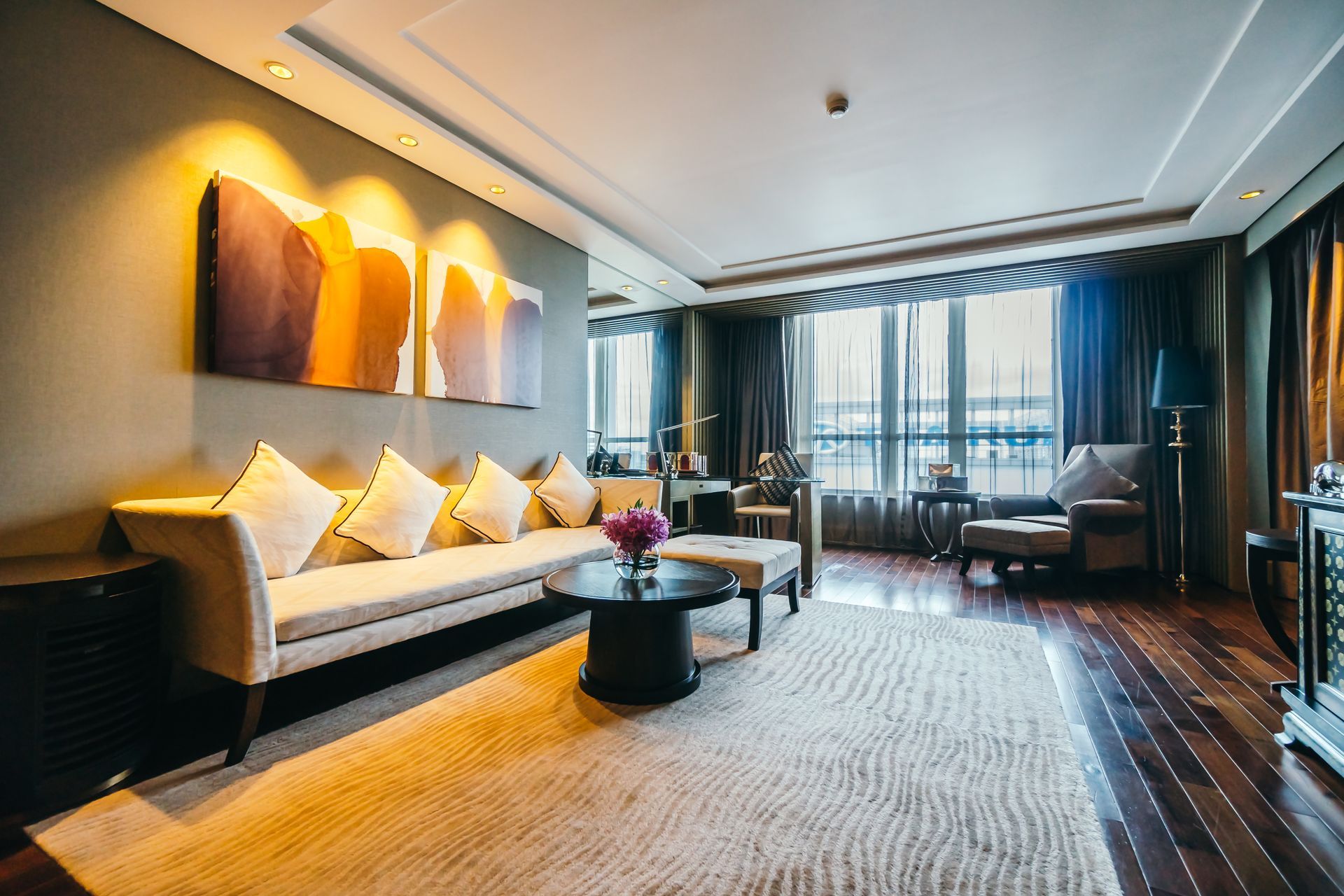 Living room with beige sofa, artwork, rug, and dark wood floors, large window.