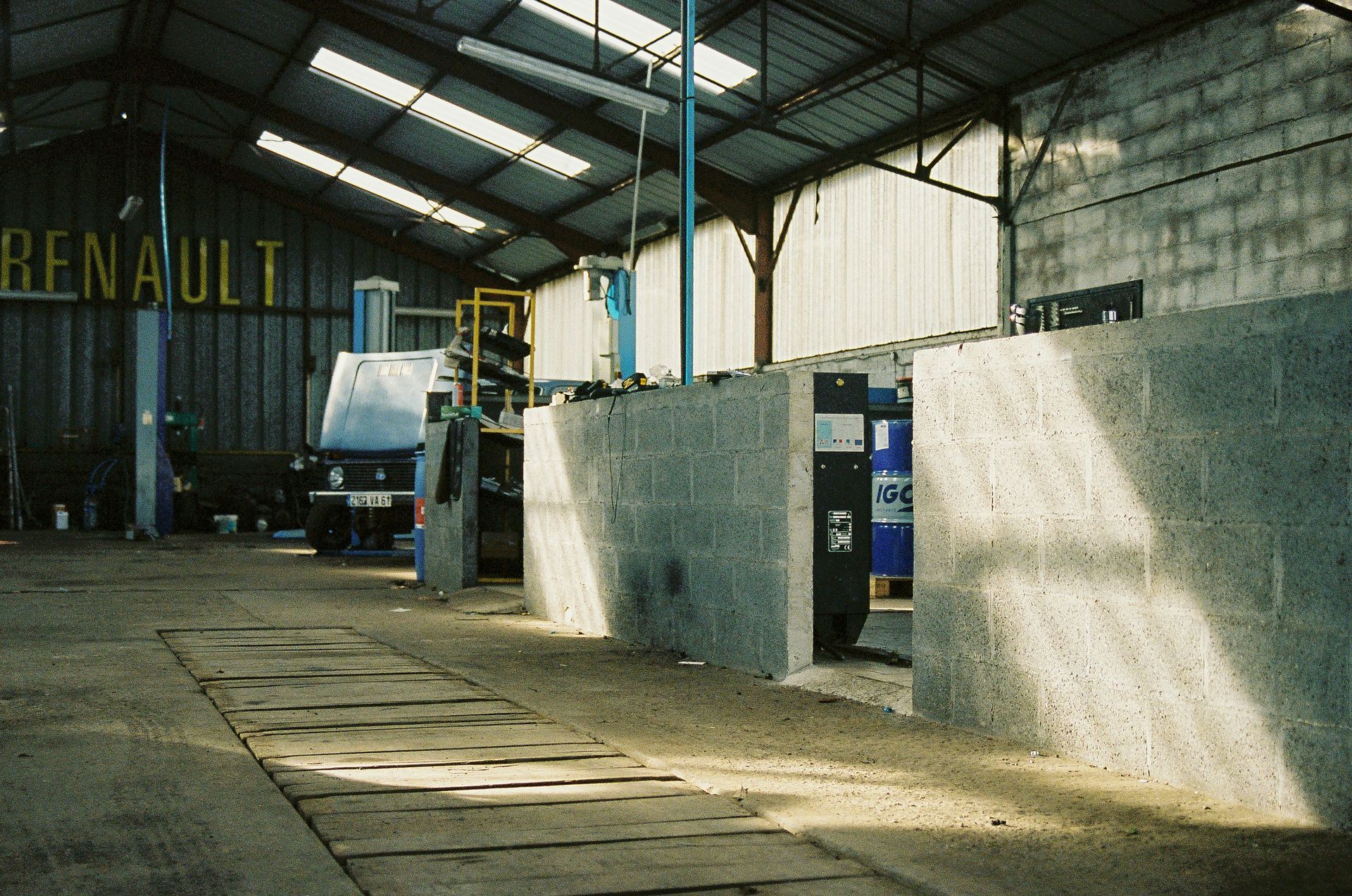 Interior of a Renault garage. Concrete blocks in the foreground, vehicles visible, and the Renault sign on the wall.