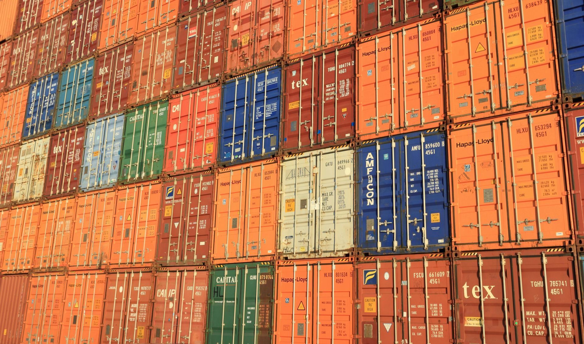Shipping containers stacked in a port; orange, red, green, blue, and white containers are visible.