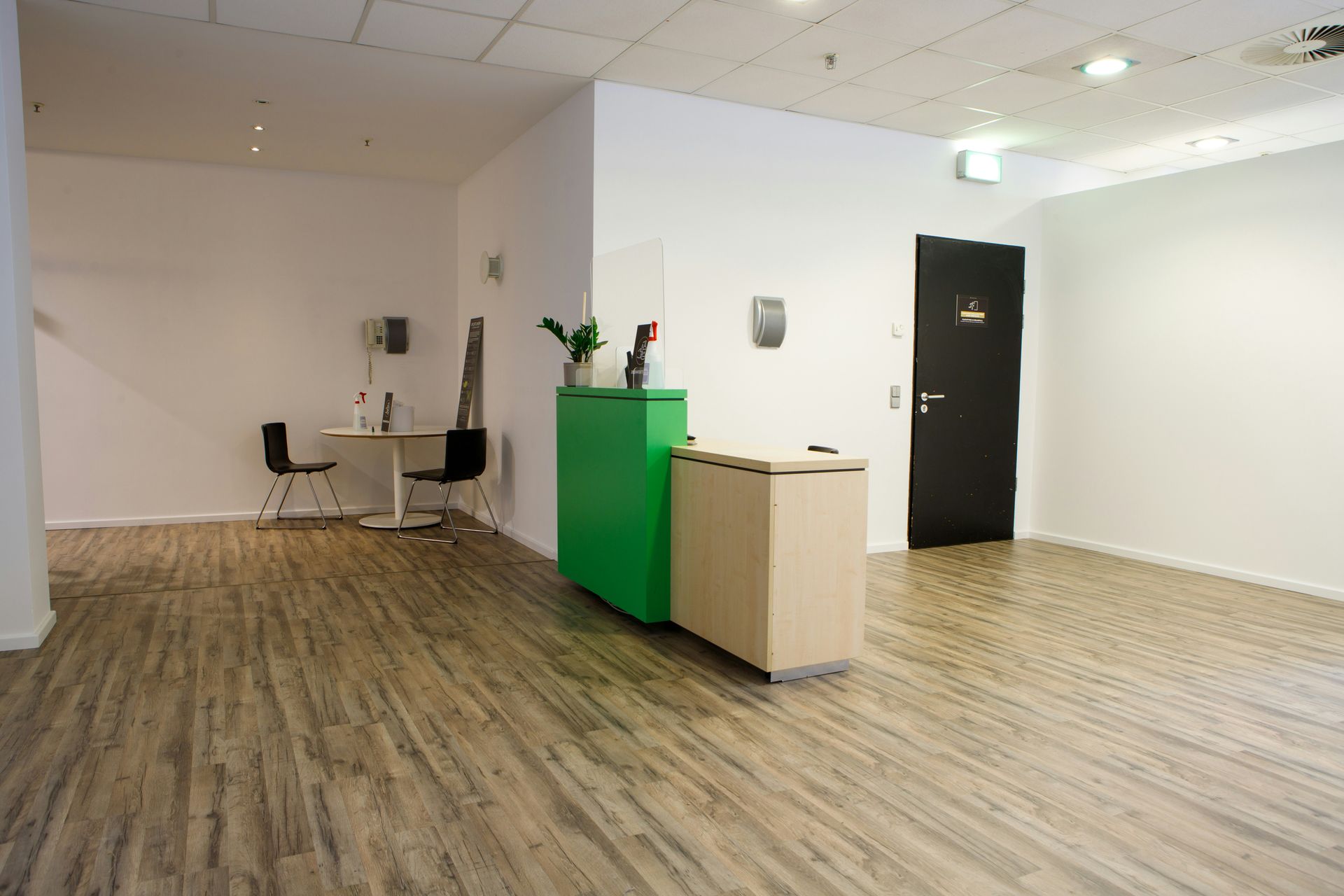 Reception area with green and beige desk, black door, and light wood flooring.