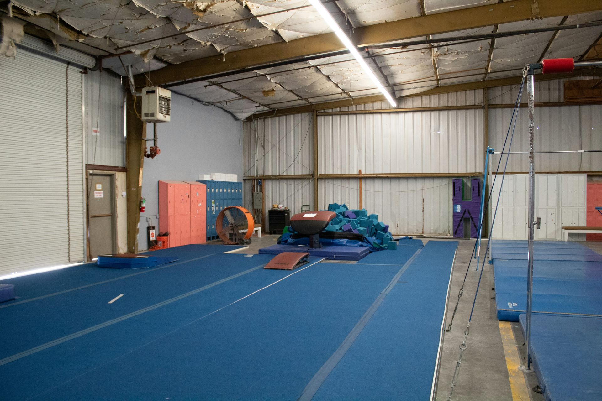 Gymnasium interior with blue mats, equipment, and exposed ceiling beams.