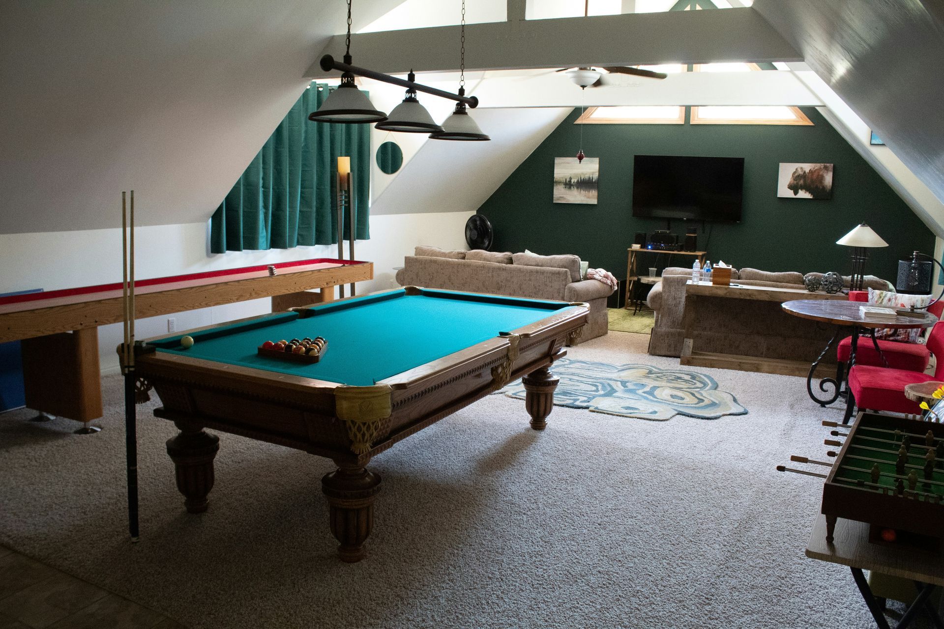 Game room with pool and table tennis tables. Teal pool table in foreground. Beige carpet and high ceilings.