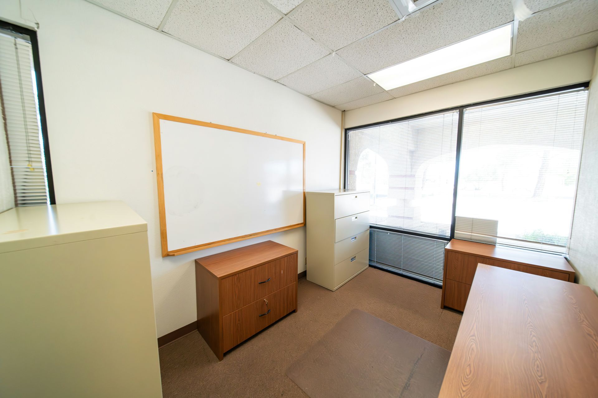 Empty office with whiteboard, file cabinets, and window.