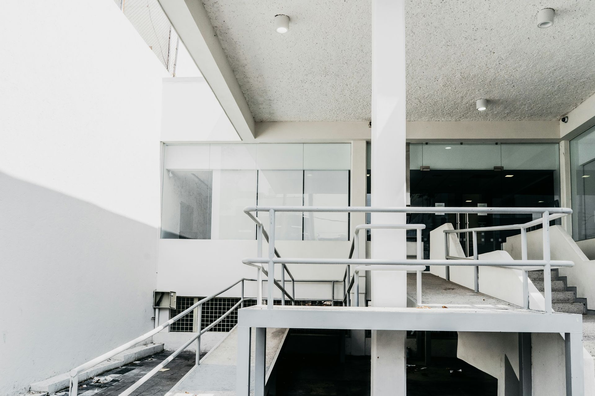 Exterior of a modern building with a ramp and stairs, painted white with glass windows.
