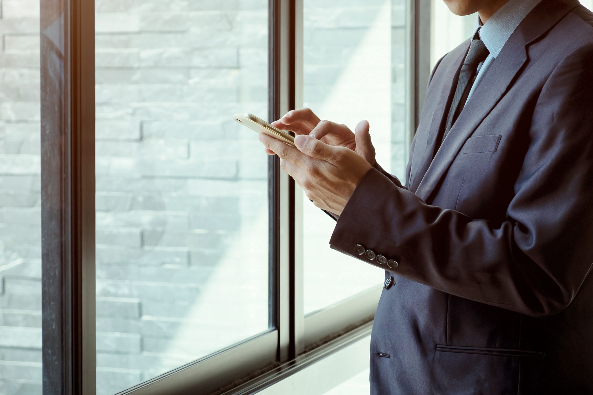 Man in suit using a smartphone near a window.