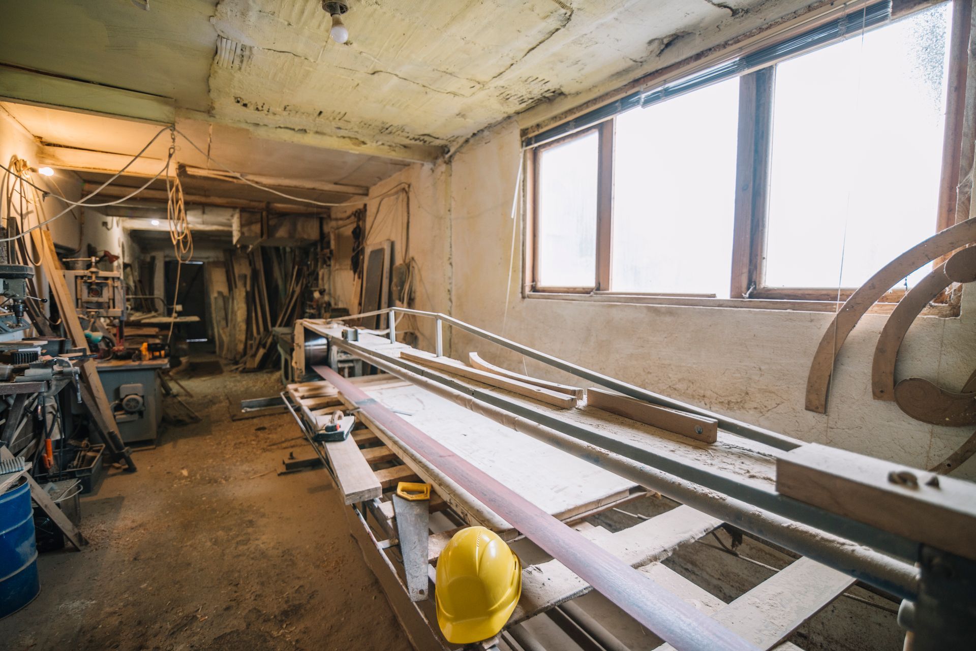 Workshop interior with woodworking tools, lumber, and yellow hard hat.