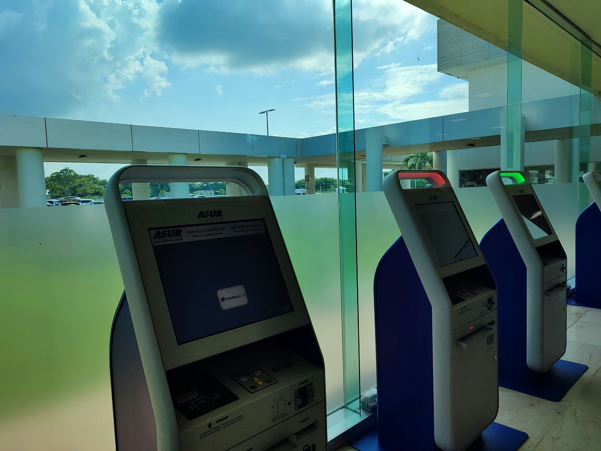ATM kiosks in a bright building with a glass wall and a view of the sky.